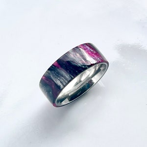 May include: A silver band ring with a black and pink marbled inlay. The inlay has a sparkly finish.
