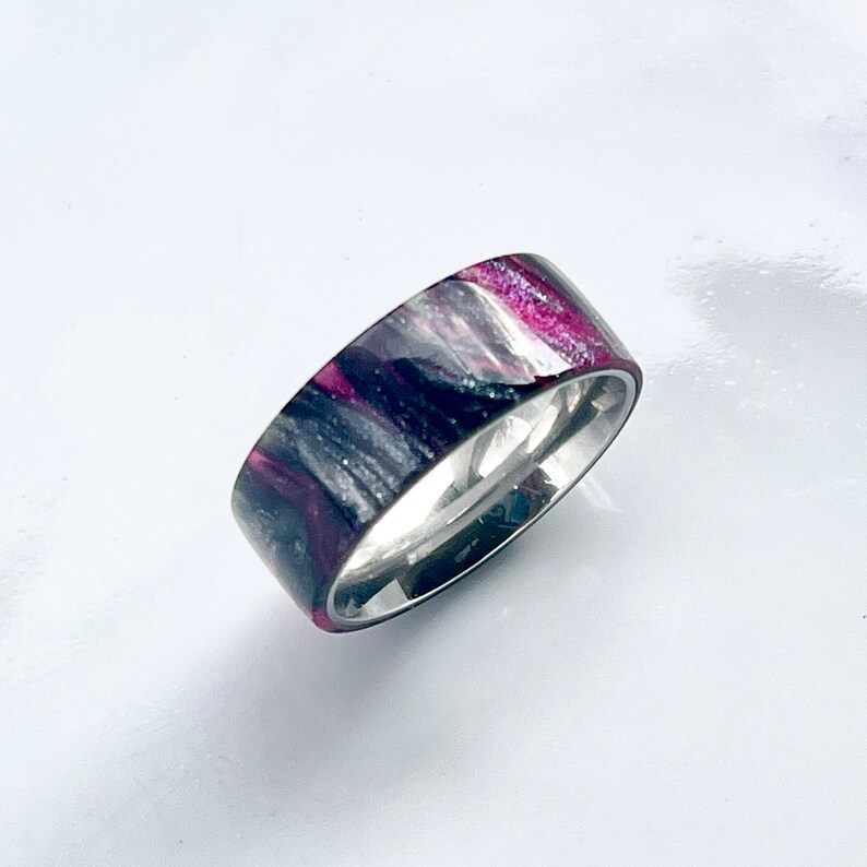 May include: A silver band ring with a black and pink marbled inlay. The inlay has a sparkly finish.