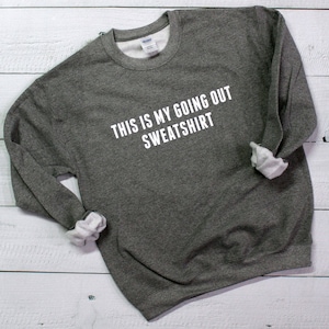 May include: A gray sweatshirt with the text "This is my going out sweatshirt" printed in white.