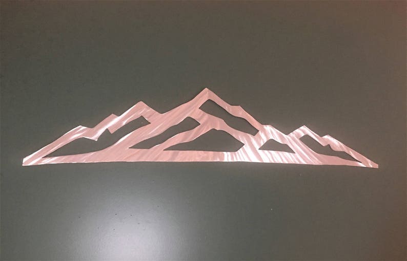 May include: A rose gold metal wall art piece featuring a stylized mountain range silhouette. The design consists of a continuous, thin, angular outline of peaks and valleys with a metallic, reflective finish and a flat, horizontal base.