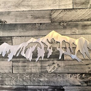 Pu&ograve; includere: Una scultura da parete in metallo argentato a forma di catena montuosa. La scultura &egrave; una silhouette di una catena montuosa con vette frastagliate. La scultura &egrave; montata su uno sfondo in legno.