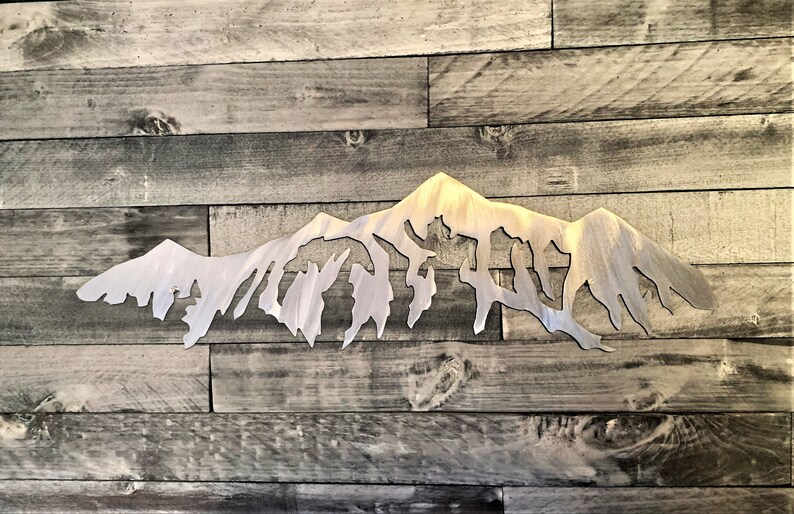 Pu&ograve; includere: Una scultura da parete in metallo argentato a forma di catena montuosa. La scultura &egrave; una silhouette di una catena montuosa con vette frastagliate. La scultura &egrave; montata su uno sfondo in legno.