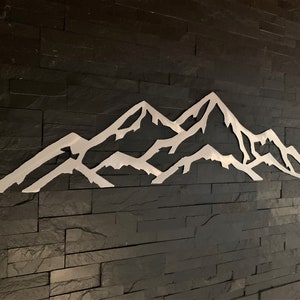 May include: A white metal mountain range silhouette wall decor on a black slate tile background.