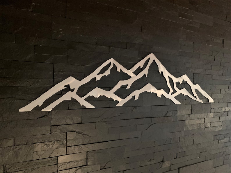 May include: A white metal mountain range silhouette wall decor on a black slate tile background.