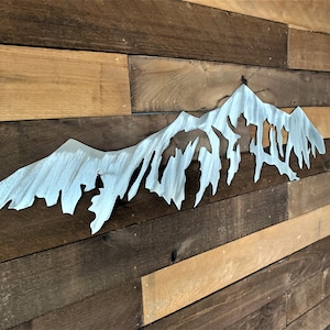 Pu&ograve; includere: Un decoro da parete in metallo argentato a forma di catena montuosa con una forma irregolare e frastagliata. Il decoro &egrave; montato su una parete in legno.