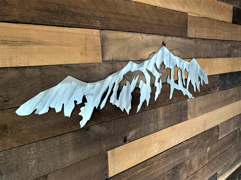 Pu&ograve; includere: Un decoro da parete in metallo argentato a forma di catena montuosa con una forma irregolare e frastagliata. Il decoro &egrave; montato su una parete in legno.