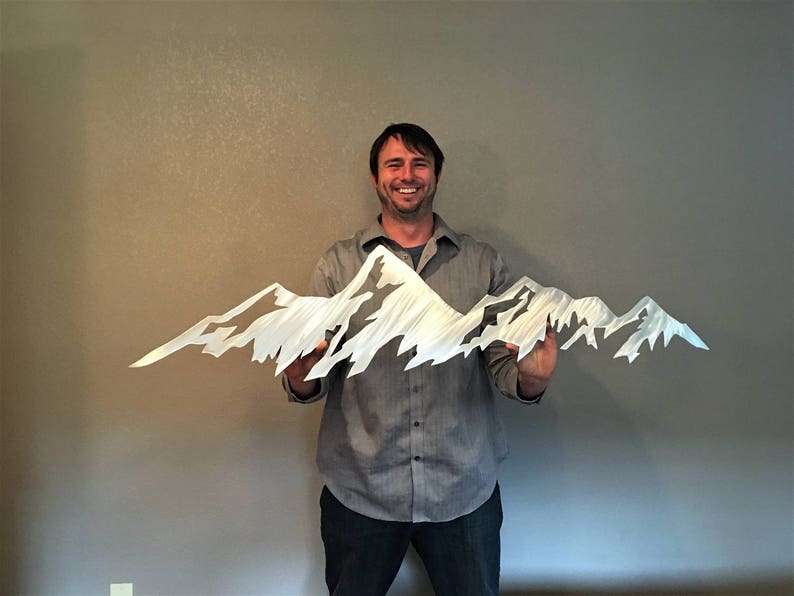 May include: A metal mountain range sculpture with a jagged, textured design. The sculpture is silver and held by a person. The artwork depicts a mountain range with peaks and valleys, suitable for home decor.