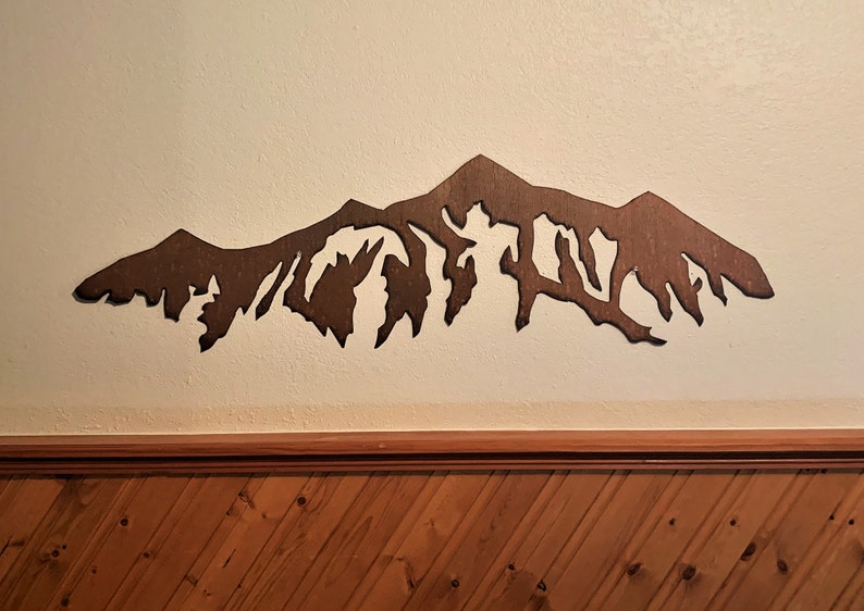 May include: A brown wooden mountain range wall decor. The mountain range is cut out of wood and has a rustic look.