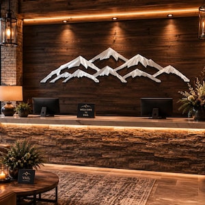 May include: A large, silver-toned metal wall art piece depicting a mountain range with multiple peaks, mounted on a dark horizontal wood-paneled wall above a reception desk. The sculpture features sharp, angular lines and a metallic finish.