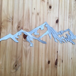 May include: A metal mountain range wall decor with a brushed silver finish. The mountain range is cut out of metal and has a realistic look.