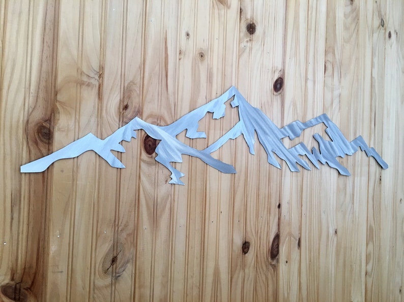 May include: A metal mountain range wall decor with a brushed silver finish. The mountain range is cut out of metal and has a realistic look.