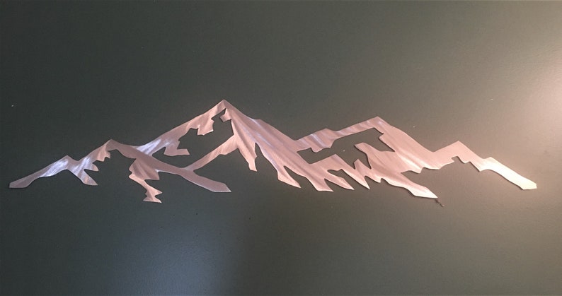 May include: A metal wall art sculpture depicting a mountain range silhouette. The sculpture is made of brushed metal and has a silver finish.