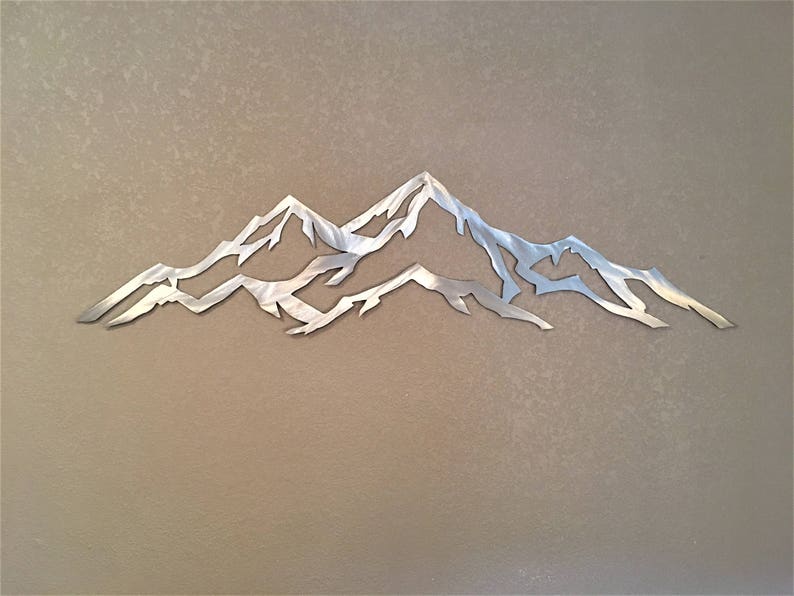 May include: A silver metal wall art sculpture depicting a mountain range with three peaks. The sculpture is cut out and has a minimalist design.