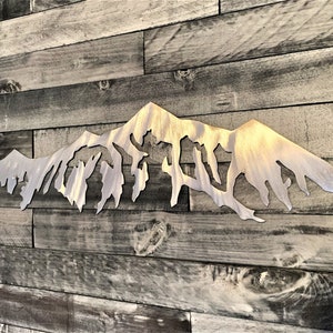 Pu&ograve; includere: Una scultura da parete in metallo a forma di catena montuosa con finitura argentata spazzolata. La scultura &egrave; montata su una parete in pannello di legno.