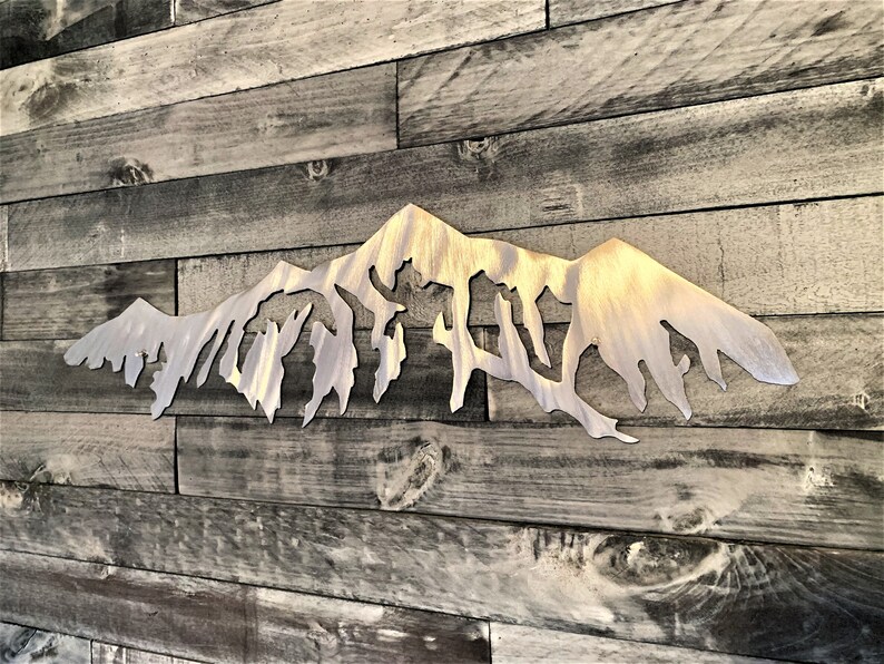 Pu&ograve; includere: Una scultura da parete in metallo a forma di catena montuosa con finitura argentata spazzolata. La scultura &egrave; montata su una parete in pannello di legno.