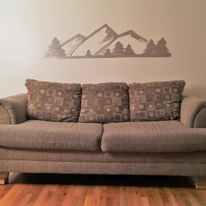 May include: A brown fabric sofa with three cushions and a mountain range wall decor above it.