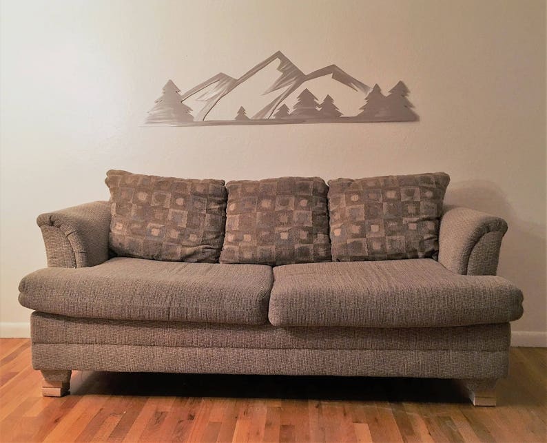 May include: A brown fabric sofa with three cushions and a mountain range wall decor above it.