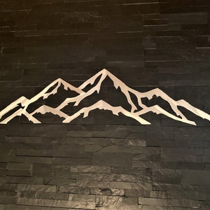 May include: A white metal mountain range silhouette on a black slate wall.