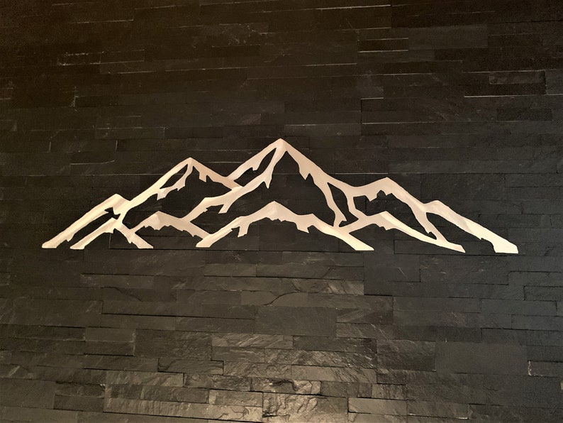 May include: A white metal mountain range silhouette on a black slate wall.