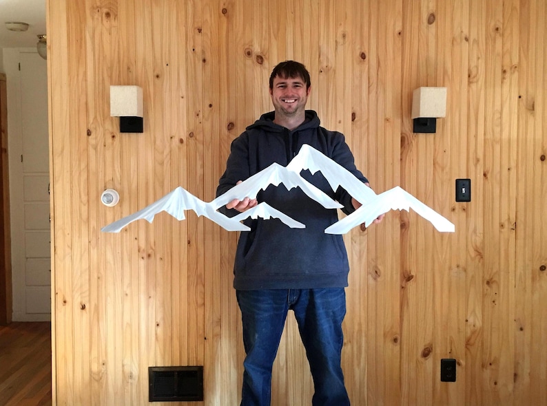 May include: A white, multi-layered mountain range wall art piece featuring jagged, snow-capped peaks. The sculpture consists of several overlapping, angular mountain silhouettes arranged in a horizontal formation, creating a layered effect.