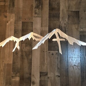 May include: A metal wall decor featuring a silhouette of three mountain peaks. The peaks are cut out of a single sheet of metal and have a brushed silver finish.