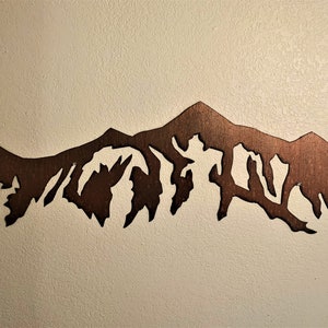 May include: A brown metal silhouette of a mountain range, cut out and mounted on a white wall.