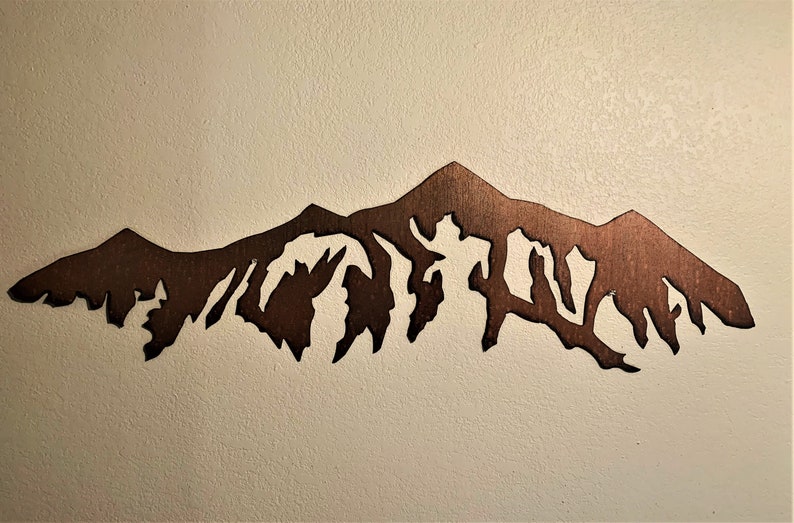May include: A brown metal silhouette of a mountain range, cut out and mounted on a white wall.