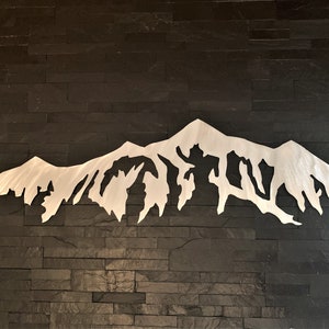 Pu&ograve; includere: Una scultura da parete in metallo argentato a forma di catena montuosa con una silhouette frastagliata e dettagliata. La scultura &egrave; montata su una parete in piastrelle di ardesia nera.