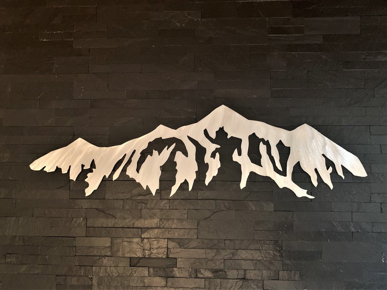 Pu&ograve; includere: Una scultura da parete in metallo argentato a forma di catena montuosa con una silhouette frastagliata e dettagliata. La scultura &egrave; montata su una parete in piastrelle di ardesia nera.