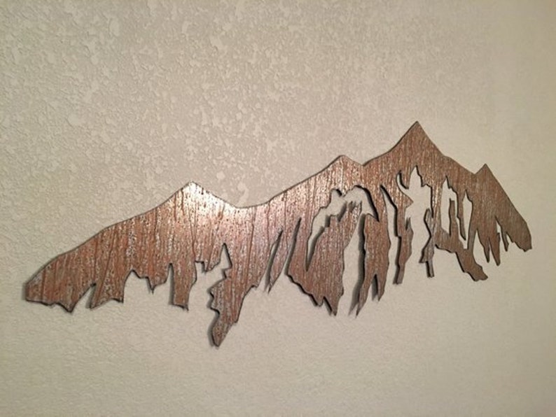 May include: A metal wall art sculpture of a mountain range with a rustic, weathered finish. The mountain peaks are cut out to create a silhouette effect.