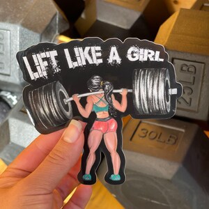 Puede incluir: Una pegatina en blanco y negro con una mujer levantando pesas. La pegatina dice "Lift Like A Girl".