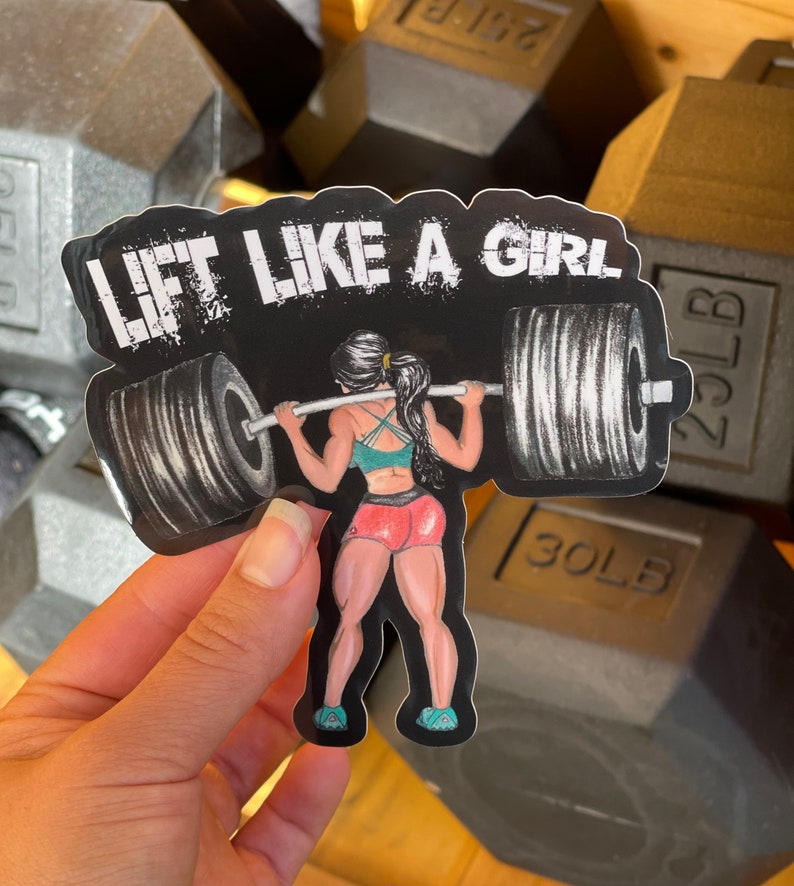 Puede incluir: Una pegatina en blanco y negro con una mujer levantando pesas. La pegatina dice "Lift Like A Girl".