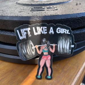 Puede incluir: Una pegatina en blanco y negro con una mujer levantando una barra. La pegatina dice "Lift Like A Girl" en letras blancas.