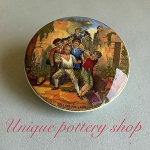 Könnte beinhalten: Ein antiker Keramikdeckel mit einer farbenfrohen Illustration einer Gruppe von Kindern, die in einem Innenhof spielen. Der Deckel ist mit einem goldenen Rand verziert und die Worte "No. Wolf and the Lamb" sind auf der Unterseite aufgedruckt.