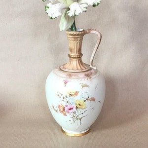May include: A white porcelain pitcher with a floral design and a single white flower with green accents.