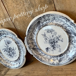 Puede incluir: Dos platos de porcelana vintage con diseños florales azules y blancos. El plato más grande tiene un borde festoneado y dos asas. El plato más pequeño es redondo.