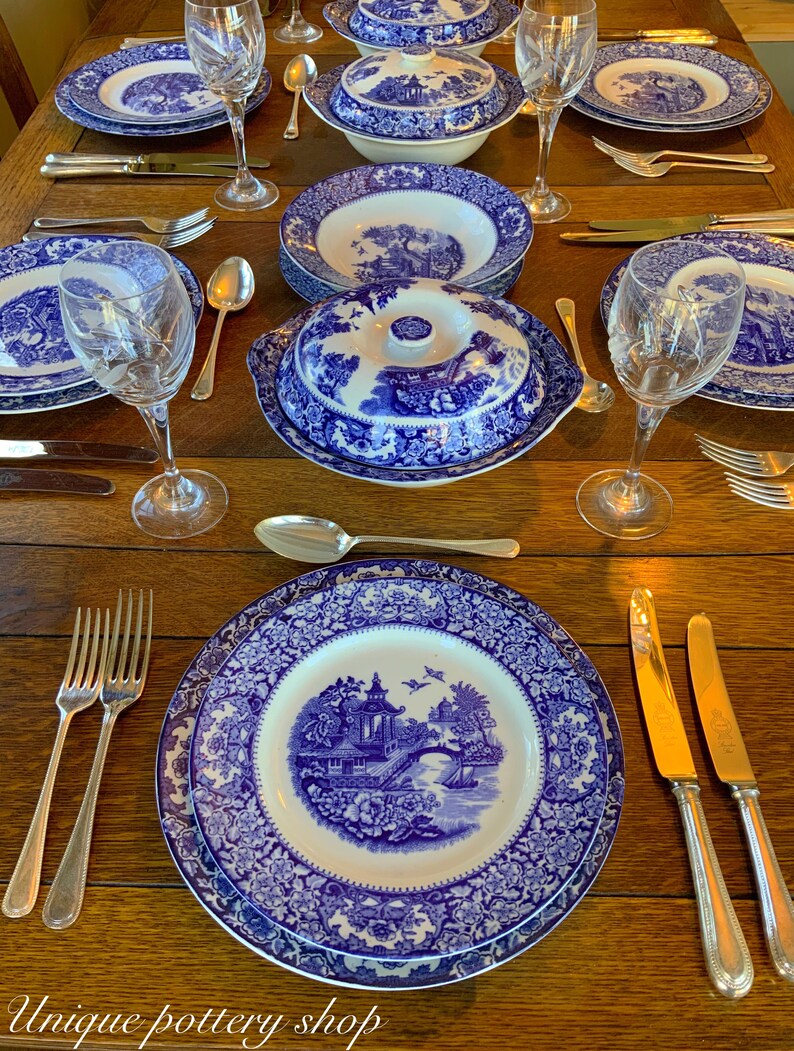 May include: A table setting featuring blue and white patterned china plates, bowls, and a serving dish. The table is laid with cutlery and wine glasses.