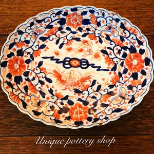 May include: A white oval ceramic plate with a scalloped edge. The plate is decorated with a blue and orange floral pattern. The pattern includes flowers, leaves, and butterflies.