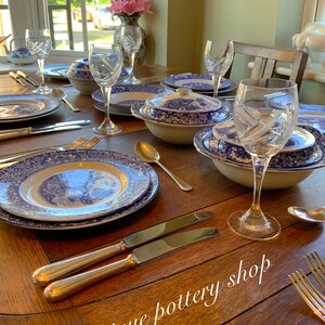May include: A wooden table set with blue and white patterned china dinnerware, including plates, bowls, and a serving dish. Crystal wine glasses and silver cutlery are also on the table. The text "Unique pottery shop" is written on the table.