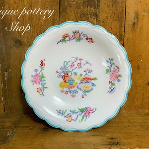 May include: A white ceramic bowl with a scalloped edge and a blue and white floral design. The bowl has a floral pattern with pink, yellow, and blue flowers.