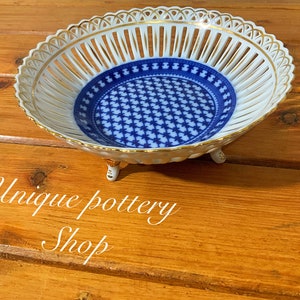 May include: A white porcelain bowl with a blue and gold pattern. The bowl has a lattice design and three gold feet.