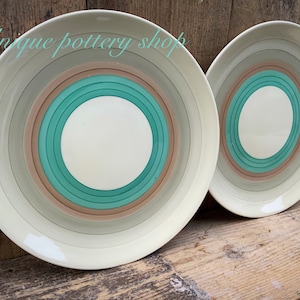 Puede incluir: Dos platos grandes de cerámica redondos con un diseño de círculos concéntricos. Los platos son blancos con círculos concéntricos marrones, beige y verde turquesa.