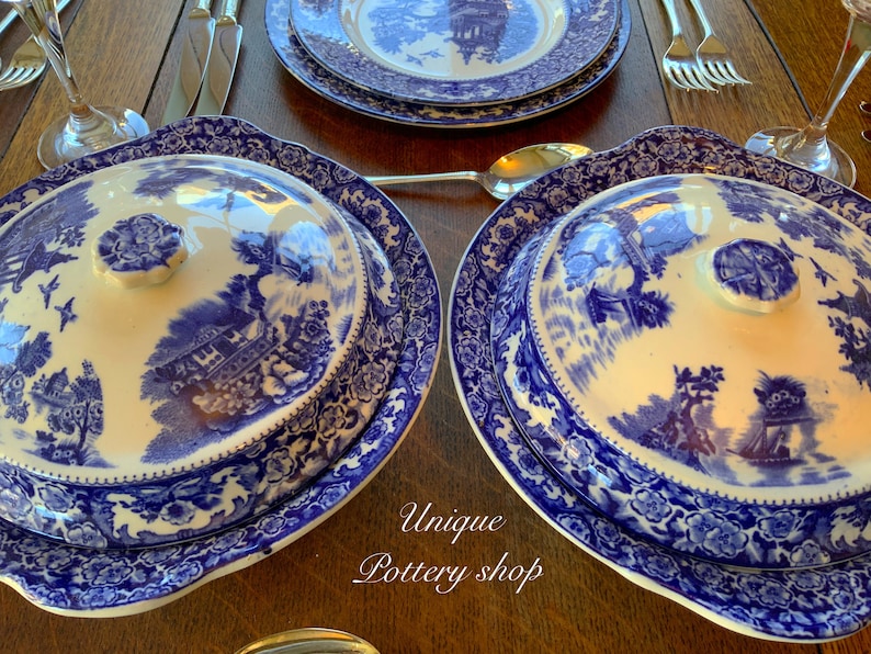 May include: Two blue and white porcelain serving dishes with lids. The dishes feature a floral pattern and a scene of a house with trees. The lids have a knob on top.