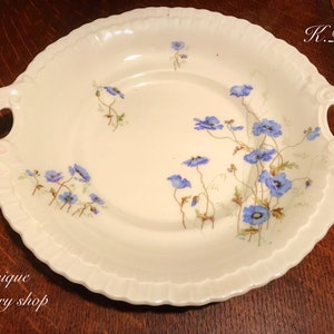 May include: A white porcelain serving dish with two handles. The dish is decorated with a blue floral pattern. The dish is oval shaped and has a scalloped edge.