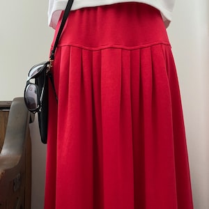 May include: A bright red pleated skirt with a fitted waistband. The skirt is made of a soft, stretchy fabric and falls to the mid-calf.