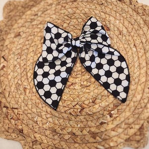 May include: A black and white bow tie with a soccer ball pattern. The bow tie is tied and ready to wear.