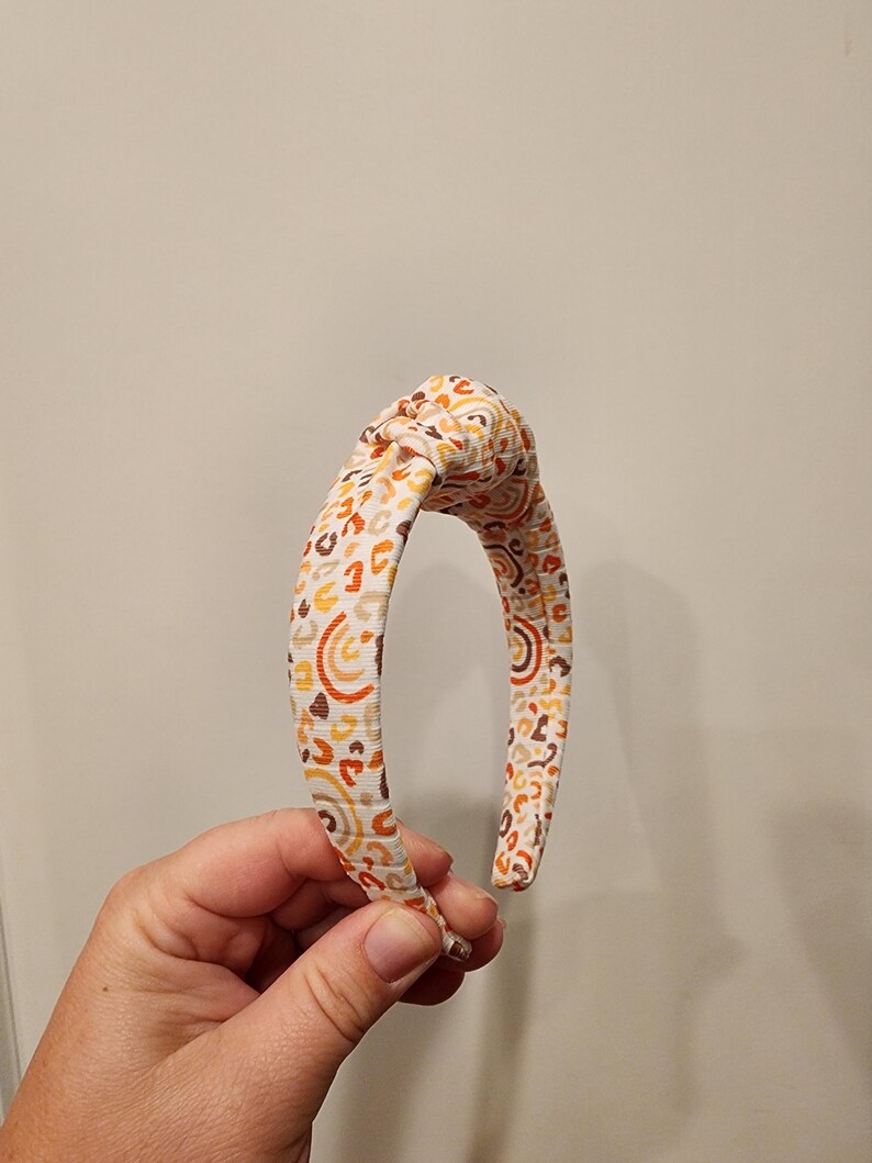 May include: A white headband with a brown, orange, and yellow abstract pattern.