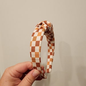 May include: A brown and white checkered headband with a knotted design.