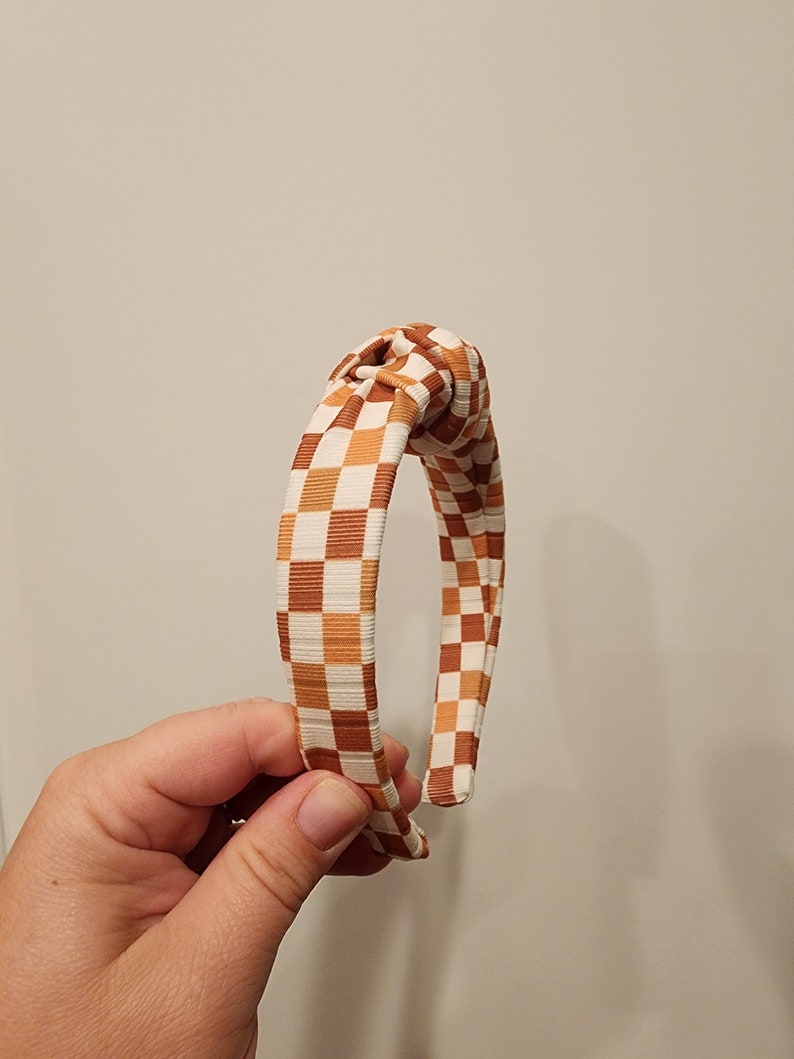 May include: A brown and white checkered headband with a knotted design.