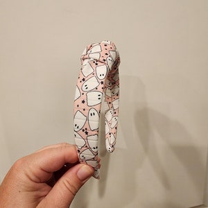 May include: A pink headband with a white ghost pattern. The headband is tied in a knot at the top.